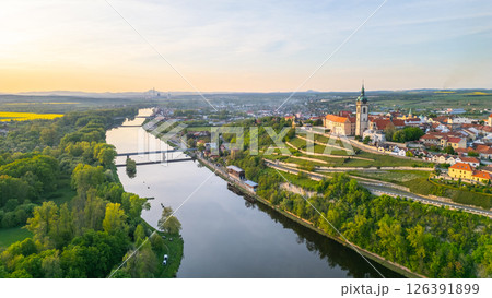 Aerial view captures Melnik City with its historic chateau above the winding Labe River. Green hills and vibrant landscapes frame the charming settlement during a serene sunset. Aerial view captures Melnik City with its historic chateau above the winding Labe River. Green hills and vibrant landscapes frame the charming settlement during a serene sunset. 126391899