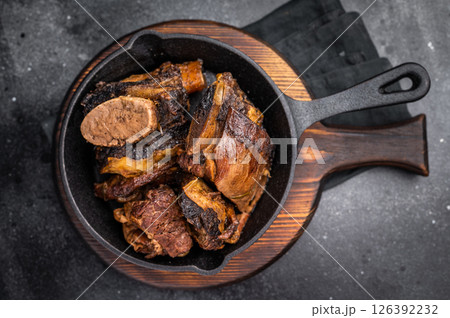Tender beef short ribs in a pan, seasoned with herbs and spices. Perfect for culinary blogs or restaurant menus that focus on hearty, flavorful meat dishes. black background. top view 126392232