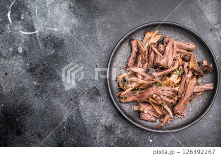 A tantalizing plate of pulled brisket, slow-cooked to perfection, drizzled with barbecue sauce for added flavor. black background. top view 126392267