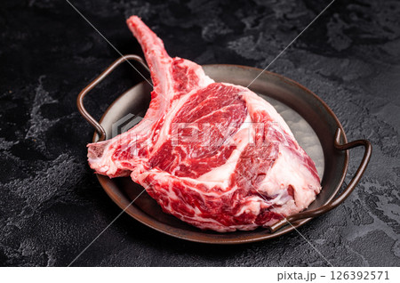 Raw tomahawk steak with marbling, fresh rib eye with bone. black background. top view Raw tomahawk steak with marbling, fresh rib eye with bone. black background. top view 126392571