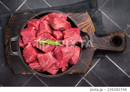 Diced Raw Ostrich meat, uncooked Game Meat in a skillet. black background. top view 126392748