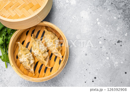 Steamed Japanese Gyoza Dumplings with pork meat and vegetables in bamboo steamer. grey background. top view Steamed Japanese Gyoza Dumplings with pork meat and vegetables in bamboo steamer. grey background. top view 126392908
