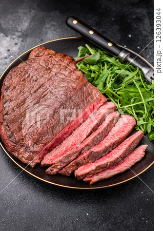 Juicy grilled top sirloin on a plate, accompanied by seasonal greens for a delicious meal. black background. top view Juicy grilled top sirloin on a plate, accompanied by seasonal greens for a delicious meal. black background. top view 126393044