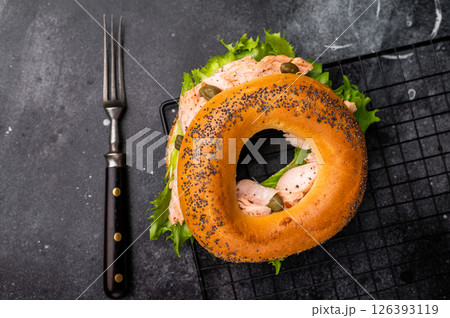 Bagel sandwich with lox, smoked salmon, lettuce and cream cheese on a rack. black background. top view Bagel sandwich with lox, smoked salmon, lettuce and cream cheese on a rack. black background. top view 126393119