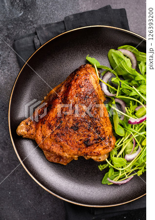 Roasted chicken thigh with salad on a plate, poultry meat. black background. top view 126393200