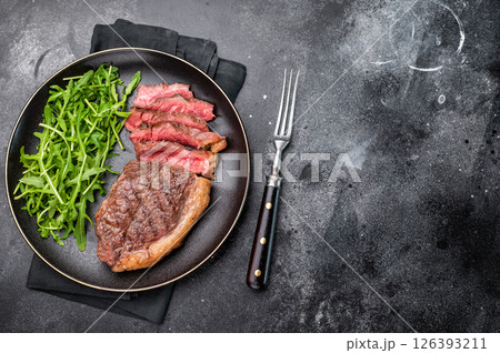 Appetizing grilled striploin steak with salad, inviting you to indulge in a mouthwatering culinary experience. black background. top view Appetizing grilled striploin steak with salad, inviting you to indulge in a mouthwatering culinary experience. black background. top view 126393211