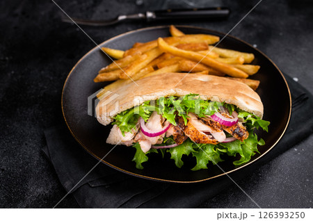 Turkish Shawarma, Doner kebab with grilled chicken meat in pita bread on a plate with french fry. black background. top view Turkish Shawarma, Doner kebab with grilled chicken meat in pita bread on a plate with french fry. black background. top view 126393250