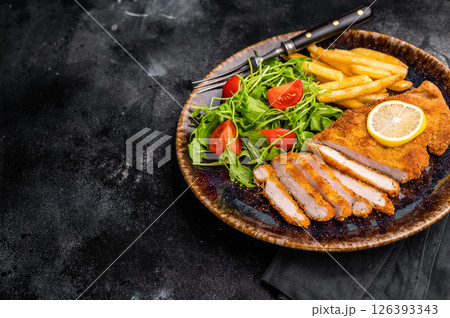 Roast viennese schnitzel steak, breaded meat with salad and french fry on a plate. black background. top view 126393343