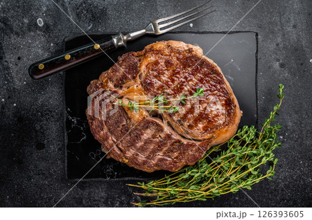 Rib eye steak with herbs on marble board, grilled prime beef meat. black background. top view Rib eye steak with herbs on marble board, grilled prime beef meat. black background. top view 126393605