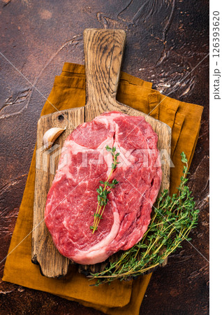 Fresh Marbled Rib eye steak with herbs on butcher cutting board, raw beef meat. brown background. top view 126393620