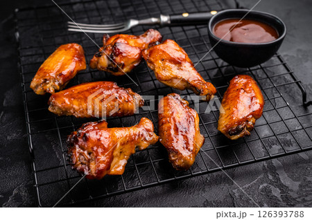 Mouthwatering BBQ chicken wings, coated in a rich sauce, perfect for finger-licking appetizers at any gathering. black background. top view Mouthwatering BBQ chicken wings, coated in a rich sauce, perfect for finger-licking appetizers at any gathering. black background. top view 126393788