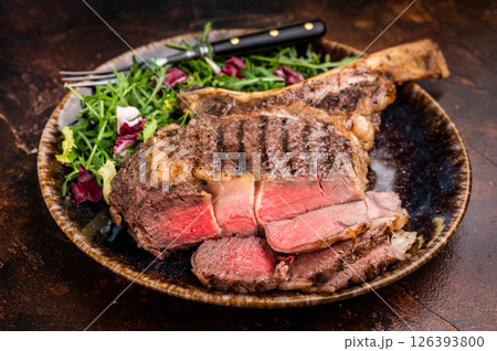 Grilled and sliced Tomahawk beef steak, marble rib eye with bone on plate with salad. brown background. top view 126393800