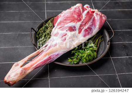 Uncooked whole goat leg, raw meat with herbs for cooking. black background. top view 126394247