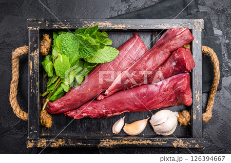 Mutton tenderloin fillet meat, raw lamb in wooden tray with herbs. black background. top view Mutton tenderloin fillet meat, raw lamb in wooden tray with herbs. black background. top view 126394667