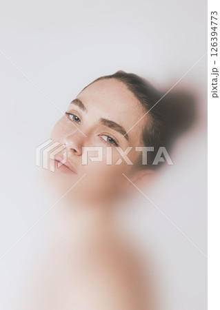 Surreal photo collage. Woman with bun looks back with soft eyes under veil of blur, calm tone and ethereal composition express fragile strength. 126394773