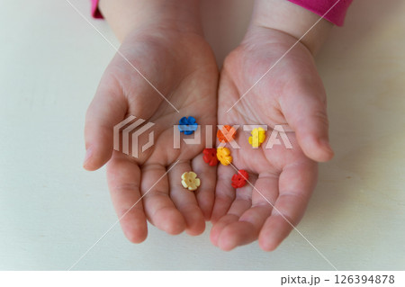 Hands of the child holding the little toys on the wood background. Colorful plastic flowers in the child hands. Hands of the child holding the little toys on the wood background. Colorful plastic flowers in the child hands. 126394878