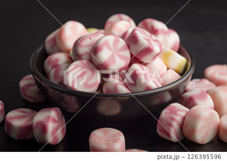 Colorful striped candies in bowl on black table. Colorful striped candies in bowl on black table. 126395596