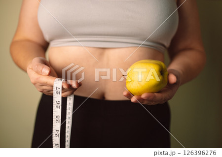 Woman holding apple and measuring tape, showing body care and health concept 126396276