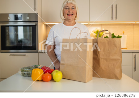 Senior woman standing in the kitchen with fresh groceries and vegetables. Senior woman standing in the kitchen with fresh groceries and vegetables. 126396278