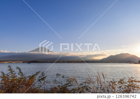 The setting sun casts a warm glow over Lake Kawaguchi, highlighting the silhouette of Mount Fuji 126396742