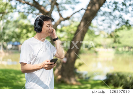 Wellness and Relaxation. Senior man enjoying music outdoors in a park with headphones. 126397059