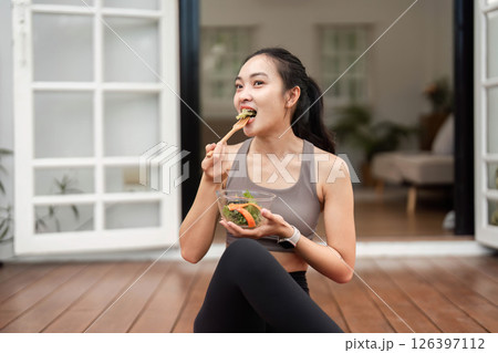 Healthy Lifestyle and Yoga. Woman enjoying a fresh salad while relaxing on a yoga mat. 126397112