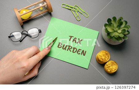 Tax burden concept. Total amount of taxes an individual or business must pay, reflecting the financial load imposed by the government. Woman points to an inscription on a notepad Tax burden concept. Total amount of taxes an individual or business must pay, reflecting the financial load imposed by the government. Woman points to an inscription on a notepad 126397274
