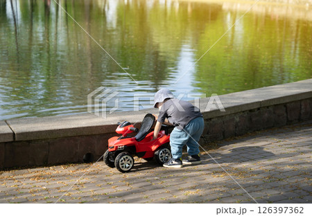 Four year old toddler boy playing with toy motorcycle near lake on sunny day. Outdoor activities, fun and games 126397362