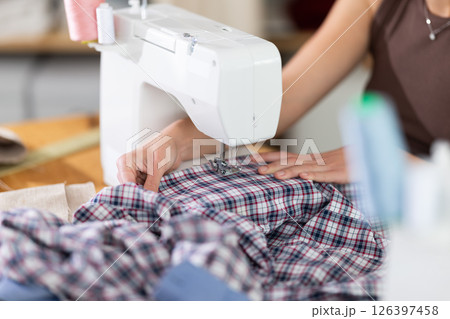 Close view of dressmaker's hands processing textile on sewing-machine Close view of dressmaker's hands processing textile on sewing-machine 126397458