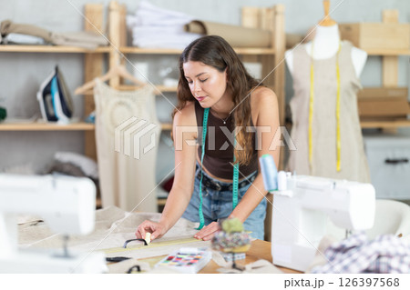 Female seamstress marking pattern lines on piece of linen with chalk 126397568