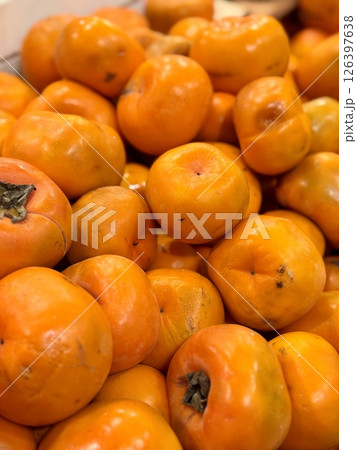A pile of ripe juicy orange flat persimmons in a box, offered for sale at a supermarket vegetable stand, demonstrates organic, vegetarian and healthy food. Close-up. A pile of ripe juicy orange flat persimmons in a box, offered for sale at a supermarket vegetable stand, demonstrates organic, vegetarian and healthy food. Close-up. 126397638