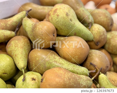 A pile of ripe, juicy green-colored pears in a box, offered for sale at a supermarket vegetable stand, demonstrates organic, vegetarian and healthy food. Close-up. 126397673