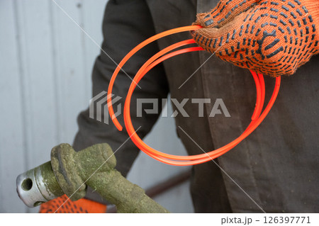 Gardening worker preparing hand trimmer for grass mowing, garden maintenance Gardening worker preparing hand trimmer for grass mowing, garden maintenance 126397771