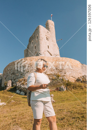 Happy old solo traveller senior woman in sunglasses with map near Mirow Castle, Poland at summer time. Happy old solo traveller senior woman in sunglasses with map near Mirow Castle, Poland at summer time. 126397806