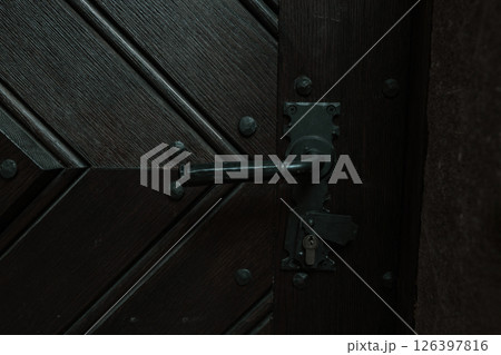 Close-Up of Vintage Wooden Door with Black Metal Handle and Diagonal Plank Design 126397816