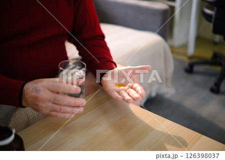 Close up of an elderly man holding a glass of water and pill Close up of an elderly man holding a glass of water and pill 126398037