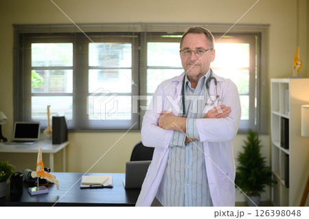 Portrait of experienced male physician with arms crossed in a bright workspace 126398048