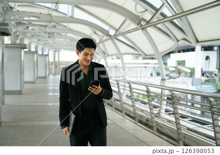 Smiling adult businessman with a phone in hand commuting to work Smiling adult businessman with a phone in hand commuting to work 126398053