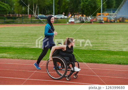 A Muslim woman in a burqa running together with a woman in a wheelchair on the marathon course, preparing for future competitions. A Muslim woman in a burqa running together with a woman in a wheelchair on the marathon course, preparing for future competitions. 126399680