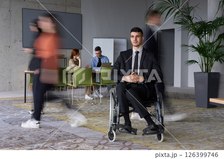 A businessman in a wheelchair navigating through a busy office, surrounded by his colleagues who are actively engaged in their work and collaboration A businessman in a wheelchair navigating through a busy office, surrounded by his colleagues who are actively engaged in their work and collaboration 126399746