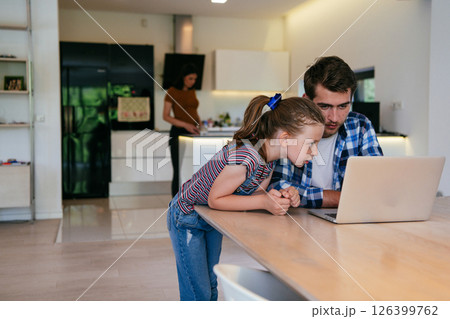 Work from home. Daughter interrupting her father while he is having a business online conversation on his laptop while sitting in the modern living room. 126399762