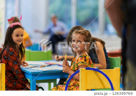 Creative kids during an art class in a daycare center or elementary school classroom drawing with female teacher. Creative kids during an art class in a daycare center or elementary school classroom drawing with female teacher. 126399769