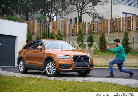 A man meticulously washes and cleans his car in the driveway of his home, showcasing pride in his vehicle and outdoor space. 126399789