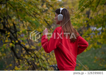 Young beautiful woman running in autumn park and listening to music with headphones on smartphone 126399801
