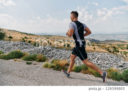 Determined Athlete Running Through Rugged Mountain Terrain at Sunrise. 126399803