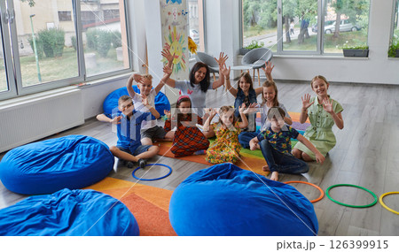 A happy female teacher sitting and playing hand games with a group of little schoolchildren A happy female teacher sitting and playing hand games with a group of little schoolchildren 126399915