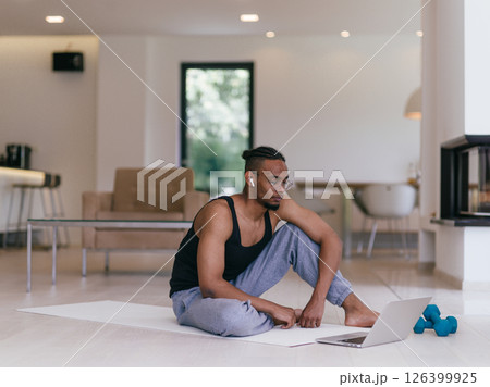 Training At Home. Sporty man doing the training while watching an online tutorial on a laptop, exercising in the living room, free space. 126399925