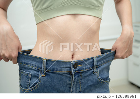 Young Asian woman losing weight wearing loose pants in oversize jeans. 126399961