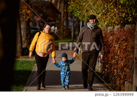 A loving couple strolls through a sunlit park with their young son, surrounded by the vibrant colors of autumn, enjoying a joyful and peaceful family moment together. A loving couple strolls through a sunlit park with their young son, surrounded by the vibrant colors of autumn, enjoying a joyful and peaceful family moment together. 126399999