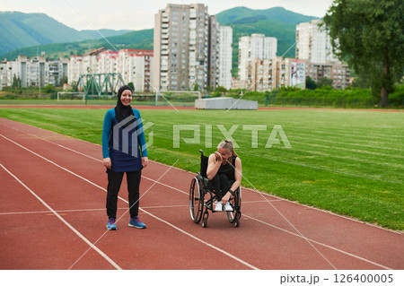 A Muslim woman in a burqa running together with a woman in a wheelchair on the marathon course, preparing for future competitions. 126400005